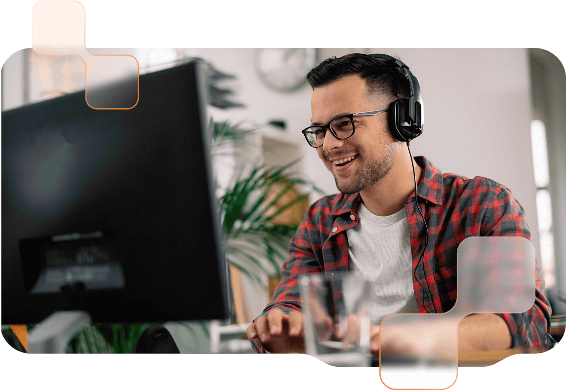 Mann mit Brille sitzt mit Headset vor einem Desktop und lächelt. 