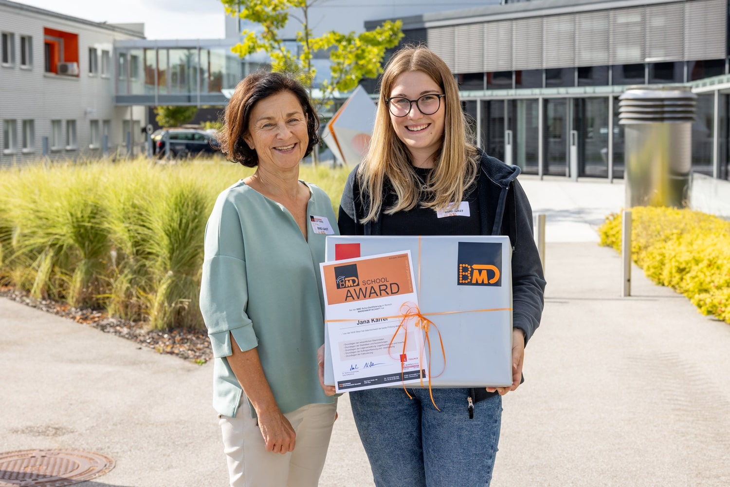 Preisträgerin des BMD School Awards präsentiert stolz ihre Urkunde und ihren Preis. Die Lehrkraft steht neben ihr.