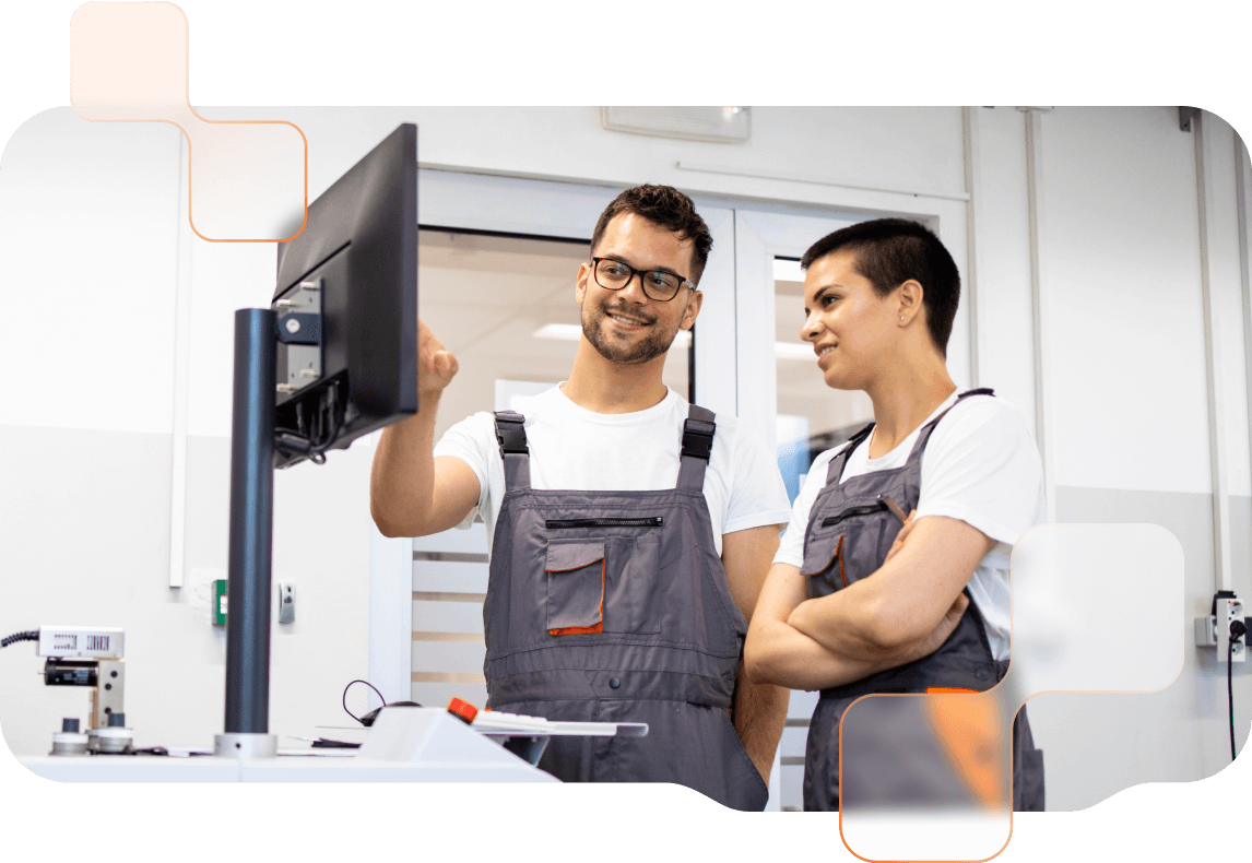 Eine Frau und eine Mann blicken in Produktionshalle auf einen Monitor. 