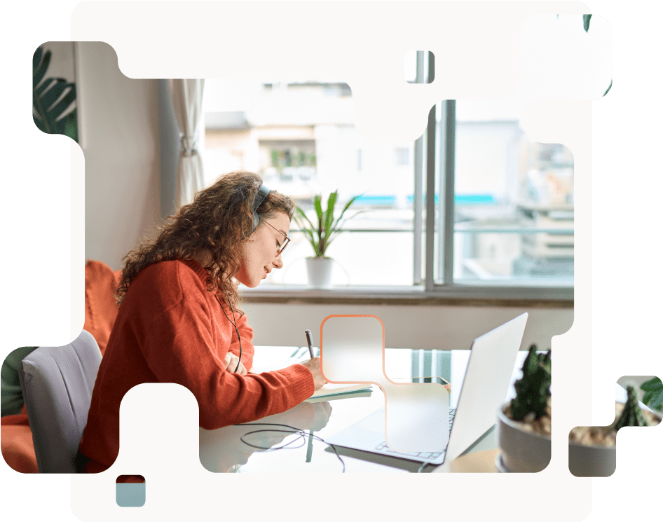 Schülerin im orangen Pullover mit Laptop am Schreibtisch sitzend und lernend.