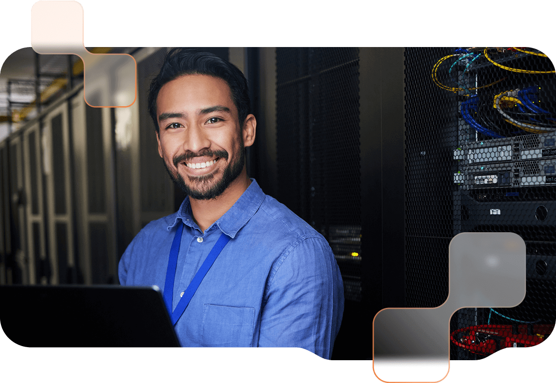 Technician in a blue shirt stands in the server room and smiles.
