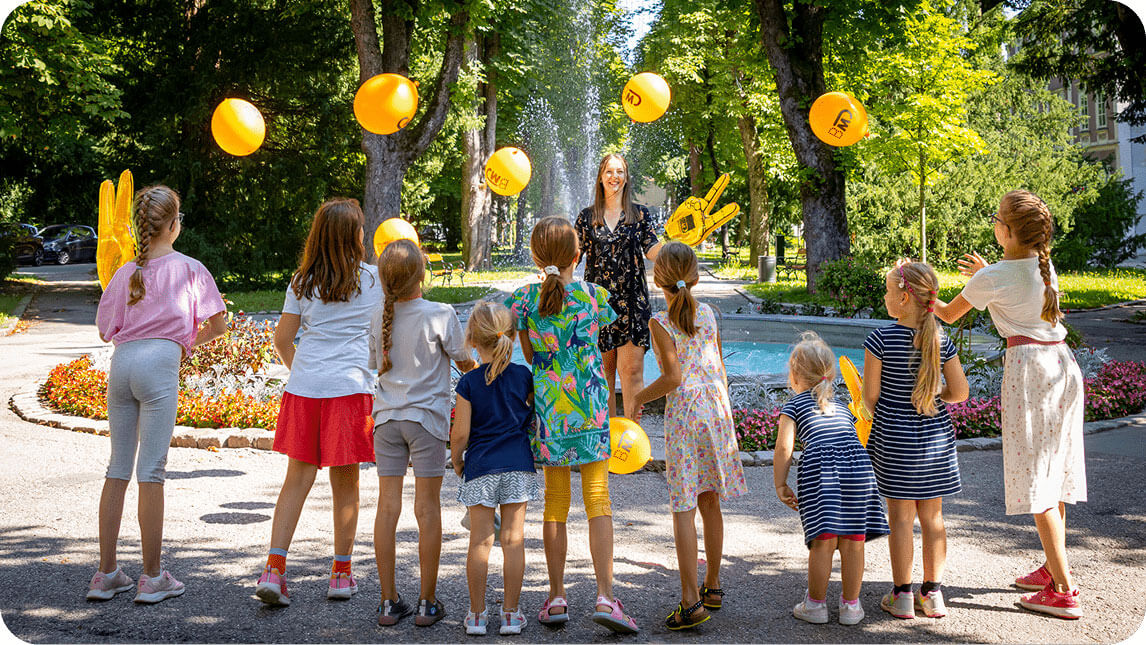 Kinder der BMD Mitarbeitenden stehen in einem Park und werfen Luftballons in die Luft.