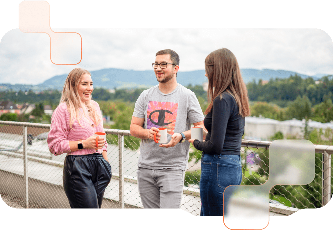 Drei BMD Mitarbeitende unterhalten sich auf der Dachterrasse des BMD Gebäudes und halten Kaffeetassen in ihren Händen.