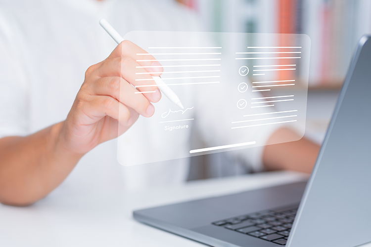 Eine Person signiert ein Dokument auf einem virtuellen Bildschirm mit einem digitalen Stift vor einem Laptop.