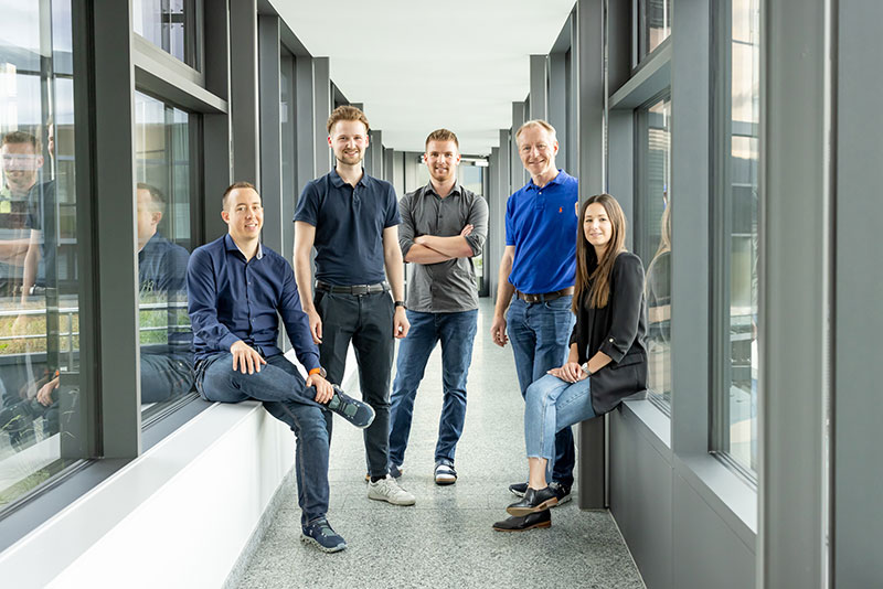 Das Bild zeigt 5 BMD Mitarbeiter und Mitarbeiterinnen, die im Bereich Finanzbuchhaltung und KI tätig sind. Sie stehen in einem Gang des BMD Gebäudes und lächeln in die Kamera.