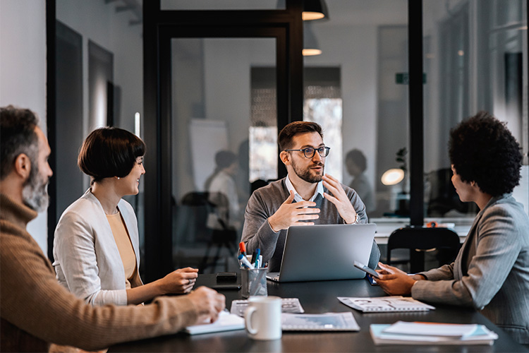 Zwei Männer und zwei Frauen sitzen an Meeting-Tisch und unterhalten sich. 
