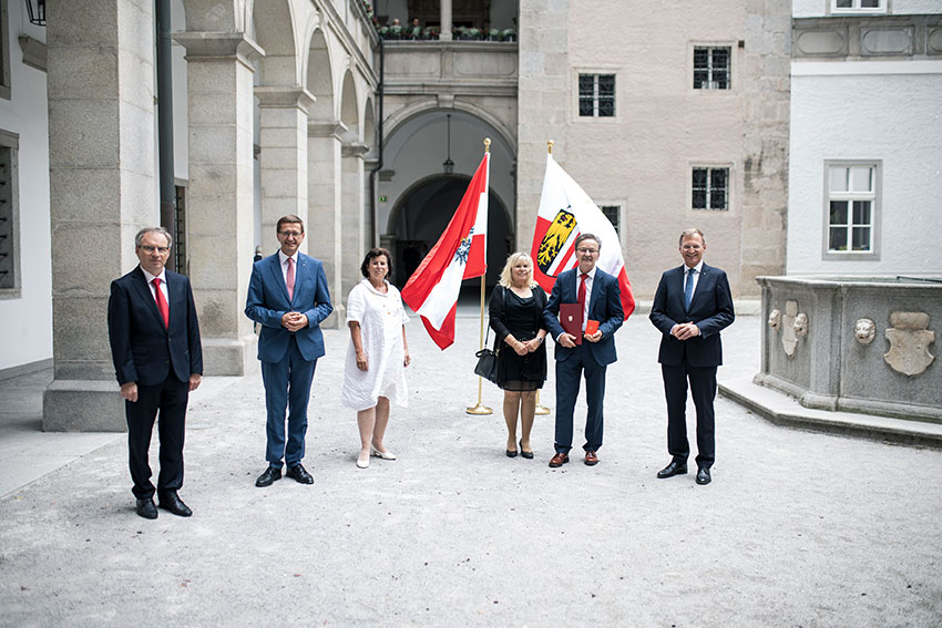 6 Personen in einem Hof vor der österreichischen und oberösterreichischen Fahne