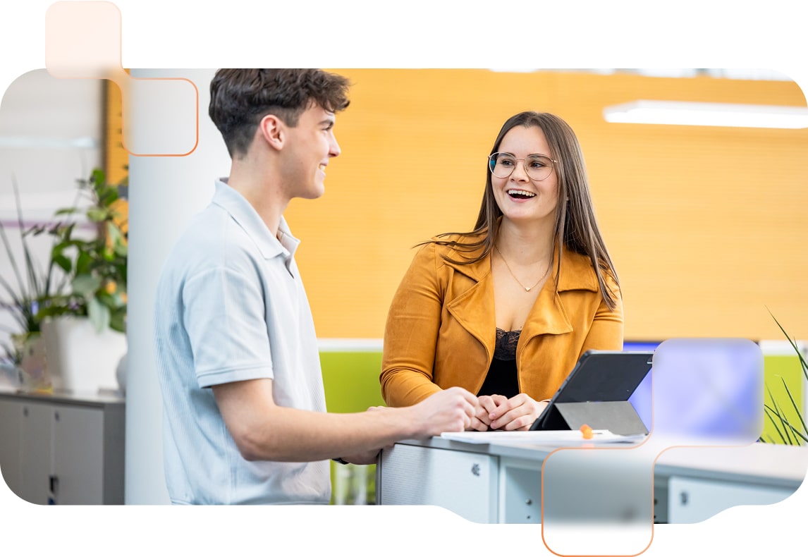 Zwei junge Personen stehen im Büro mit einem Tablet und haben Spaß beim Arbeiten.