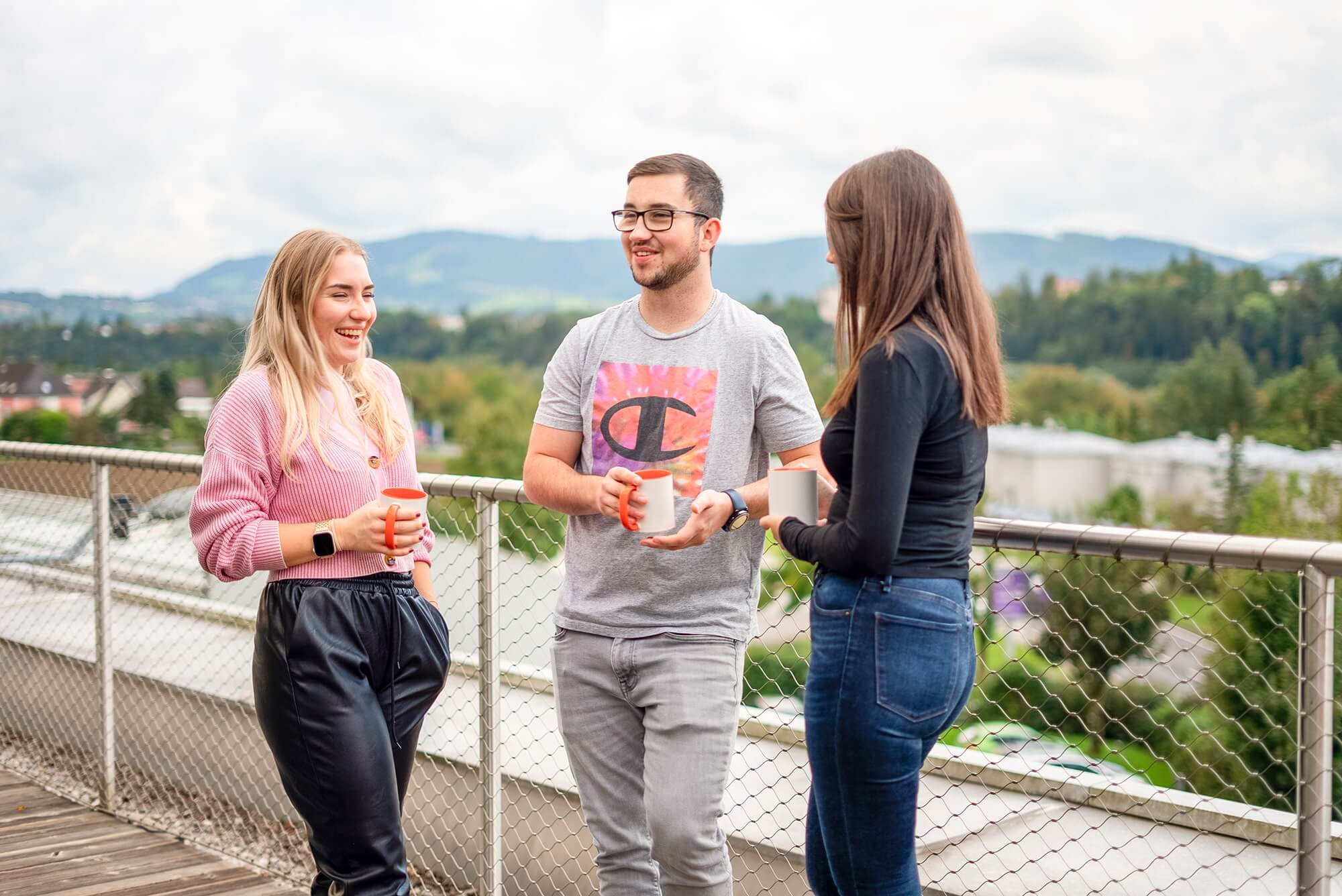 Drei Personen stehen auf der Dachterasse und halten Kaffeetassen in den Händen.