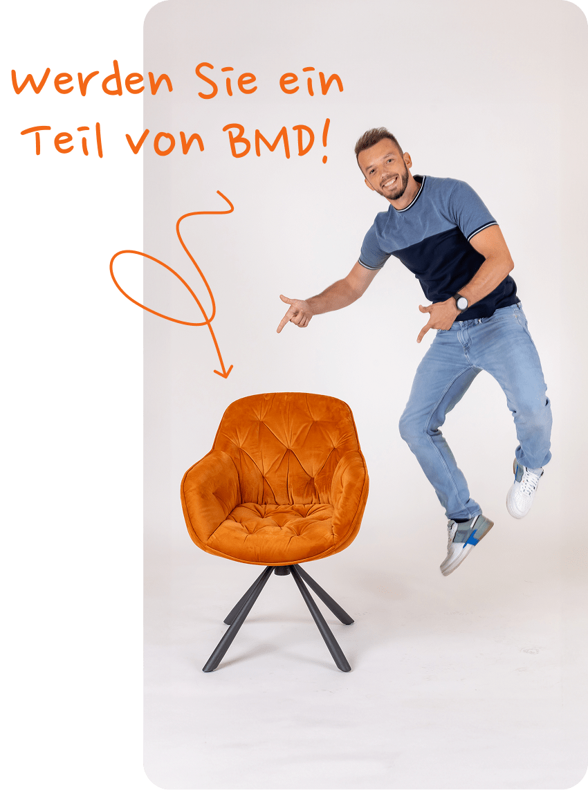 Ein junger Mann springt in die Luft und zeigt auf einen orangen Sessel.