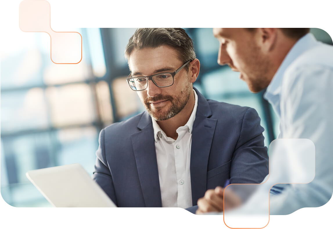 Zwei Männer im Business-Outfit sitzen fokussiert vor einem Tablet. Dahinter moderne Büro-Umgebung.